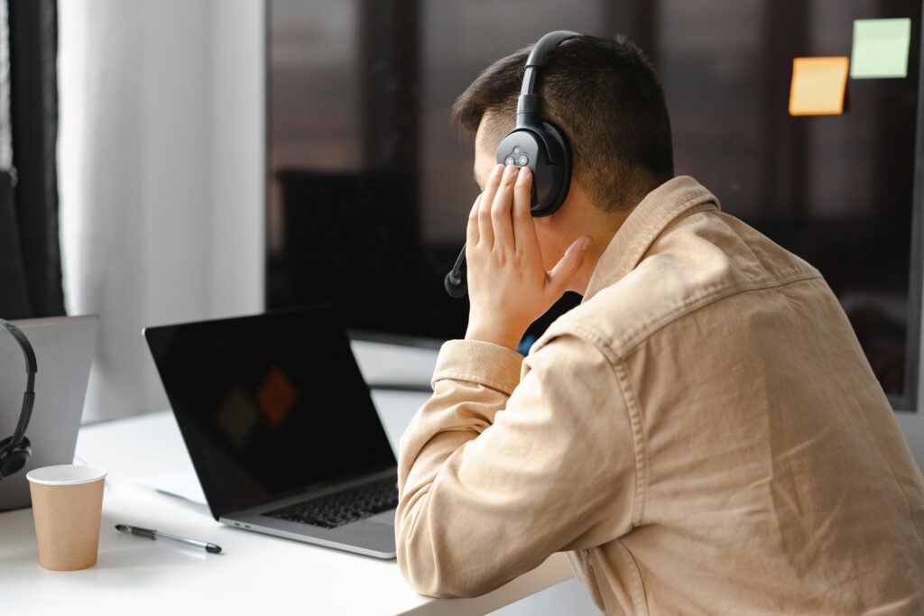 pexels-photo-7681302-7681302 A man wearing headphones works at a laptop in a modern office setting.